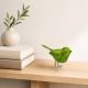 Petit oiseau en métal vert présenté sur une console claire