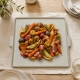 Plat de service carré Notos crème garni de légumes rôtis sur une table en bois clair.
