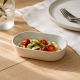 Petit plat ovale Nótos crème garni de légumes rôtis sur une table en bois clair