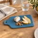 Planche bleu pétrole avec fromage de chèvre, poire et noix sur une table en bois clair.