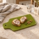 Planche verte avec tartines au chèvre et radis, accompagnées de noix sur une table en pierre claire.