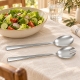 Couverts à salade en inox poli près d’un saladier de crudités sur une table en lin clair.