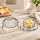 Cloche Versailles à côté d’une coupelle garnie de beurre sur une table en pierre claire avec du lin et de la brioche.
