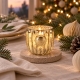 Photophore Dante doré allumé sur une table de Noël avec lin, sapin et ornements de papier.
