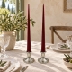 Duo de bougeoirs argentés avec bougies flambeaux rouges et nappe damassée ivoire, pour une table élégante.
