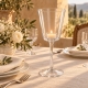 Photophore conique en verre avec une bougie allumée sur une table en lin naturel, accompagnée de vaisselle blanche et de fleurs.