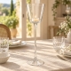 Photophore sur pied en verre avec une petite bougie allumée, sur une table en lin naturel et vaisselle blanche.