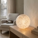 Lampe boule blanche et dorée allumée sur une console en bois patiné.